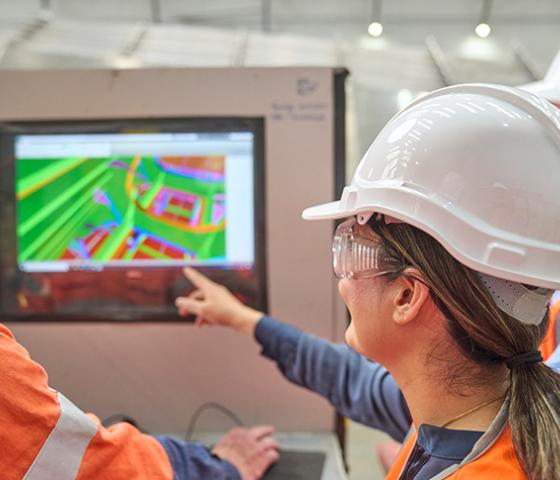 Person wearing hivis and a hard hat pointing to a project screen