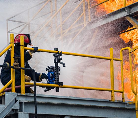 Fire fighter standing on a platform using a fire hose to fight a fire