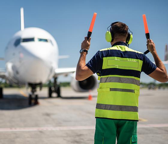 Image of an aviation grounds operator directing a plane 