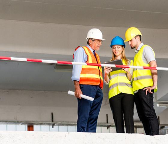 Image of 3 building supervisors, wearing hivis and hard hats, looking at a tablet device