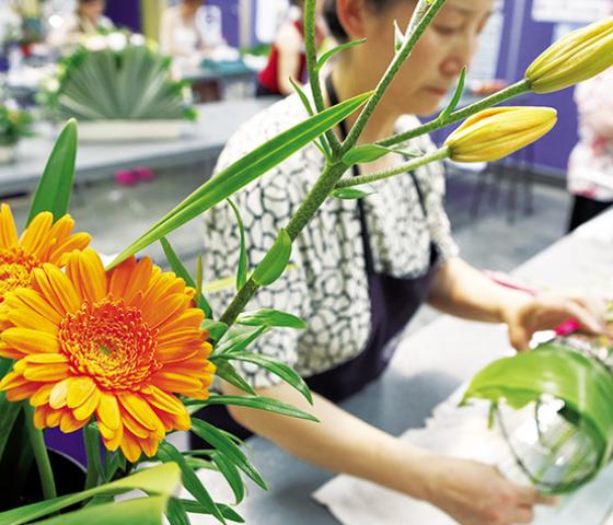 Close up of orange flowers with a blurred person behind wearing an apron and working with flowers